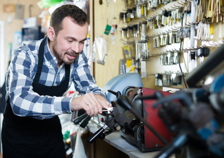 Smiling male worker shaping new key in repair workshopの写真素材