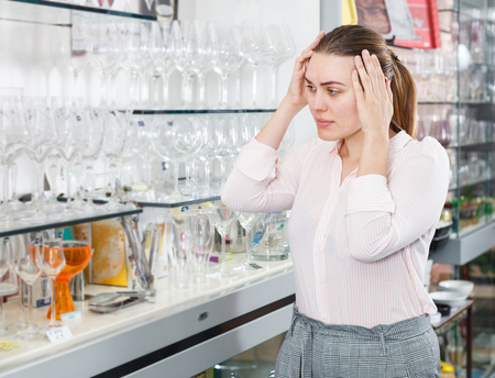 Young worried female customer choosing wineglass in the tableware storeの写真素材