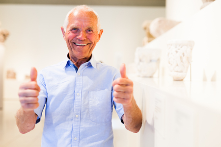 Happy mature man satisfied by visiting museum and showing thumbs upの写真素材
