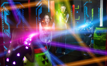 Group of happy kids and adults having fun on dark lasertag arena in colorful beams of laser guns