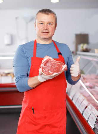 Positive man  seller demonstration quality meat in butcherâs shopの写真素材