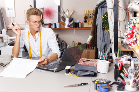 Professional male tailor at work â creating pattern using laptop and graphics tablet at his workplaceの写真素材