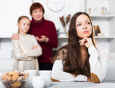 Chagrined young woman having conflict with little daughter and motherの写真素材