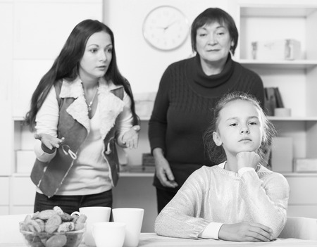 Portrait of upset little girl scolded by mother and grandma at homeの写真素材
