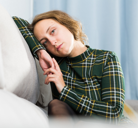 Portrait of sad girl sitting in living room at homeの写真素材