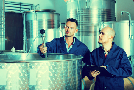 mature and young experts men standing with clipboard in wine processing sectionの写真素材