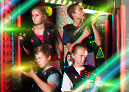 Cheerful teen girls and boys with laser pistols posing together in dark laser tag labyrinthの写真素材