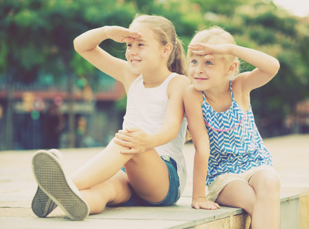 Two little cheerful girls looking at something interesting into distance outdoorsの写真素材