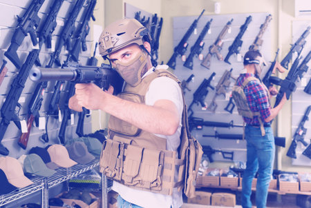 Young positive spanish guys in military equipment with rifle in airsoft shop