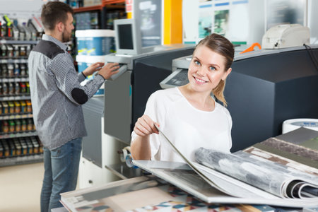 Cheerful woman looking samples of wallpaper at magazine in household store