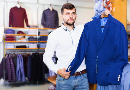 Happy cheerful  smiling handsome adult guy  choosing modern jacket in men storeの写真素材