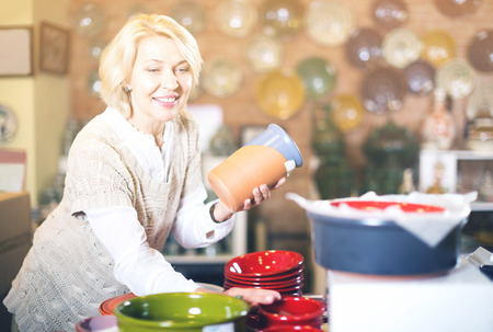 Beautiful mature woman posing with ceramic tableware at workshopの写真素材