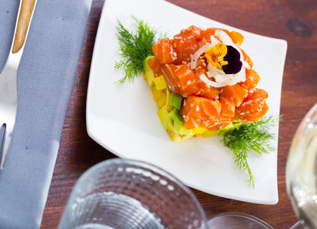 Raw salmon tartare with avocado served on white plate garnished with heartsease flower, onion and fresh dillの写真素材