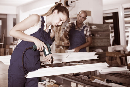Portrait of serious workwoman using electric drill on plastic window frame at factoryの写真素材