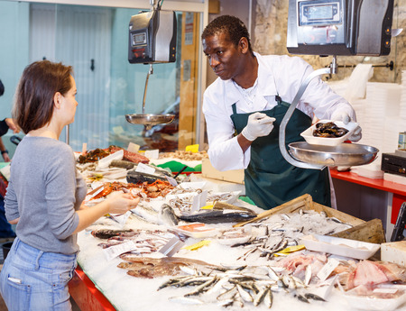 Smiling salesman proposing young woman raw clams at fish marketの写真素材