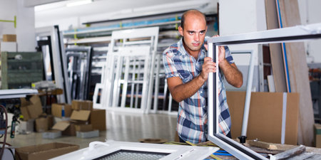 Man is checking quality of work on assembling plastic windows at factory.の写真素材