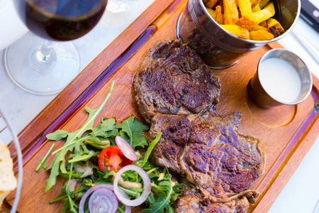 Juicy slices of roasted beef served with arugula, vegetables and sauce on wooden boardの写真素材