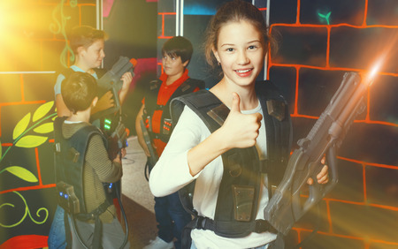Cheerful  smiling teen girl standing with laser pistol in dark lasertag room during game with friendsの写真素材