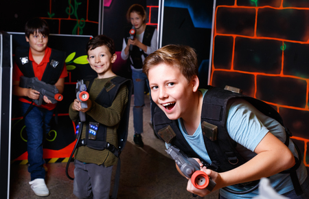 Emotional  cheerful  smiling teen boy with laser pistol playing laser tag with friends on dark labyrinthの写真素材