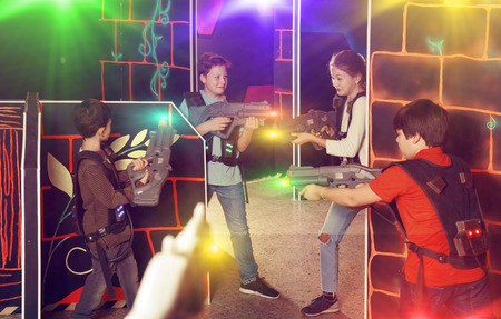 Glad teen kids aiming laser guns at other players during lasertag game in dark roomの写真素材