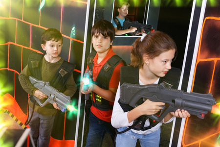 Group of cheerful friendly  smiling  teenagers with laser guns having fun on dark lasertag arenaの写真素材