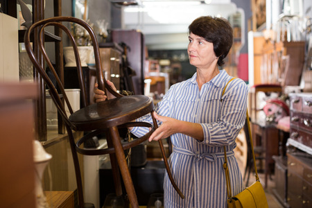 Mature female is choosing old armchair for home in antique shop.の写真素材