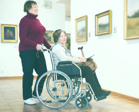 Elderly woman and positive senior disabled friend in art gallery