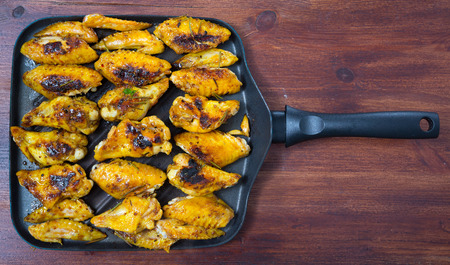 Top view of roasted chicken wings with spicy mustard sauce served on frying pan on wooden backgroundの写真素材