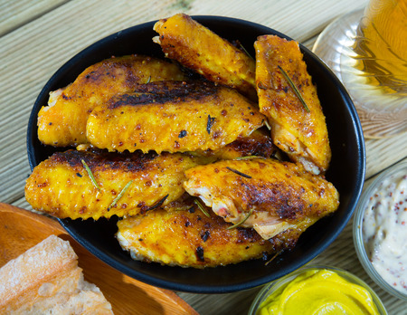 Fried chicken wings served in black bowl, two sauses and bread on tableの写真素材