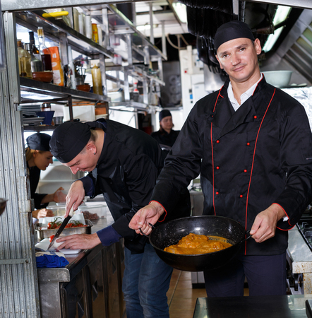 Cheerful cooks dressed in black uniform at restaurant kitchenの写真素材