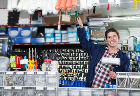 Happy adult man standing near the counter and selling rollers for repair and pantingの写真素材