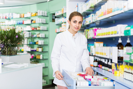 Female specialist is attentively looking medicines in lockers in pharmacyの写真素材
