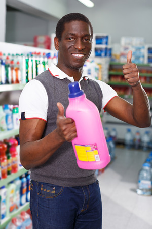 glad young African man choosing household chemicals in storeの写真素材