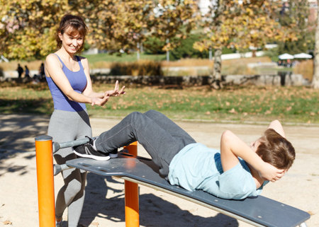 Smiling athletic woman helping tweenager boy during workout doing press up exercises