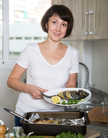 Positive housewife cooking dorado fish in baking dish at kitchenの写真素材