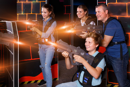 joyous young parents and children with laser pistols playing laser tag in dark labyrinthの写真素材