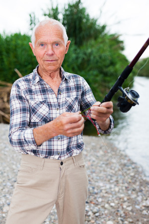 Positive adult man with rod relaxing and enjoying fishing by lakesideの写真素材