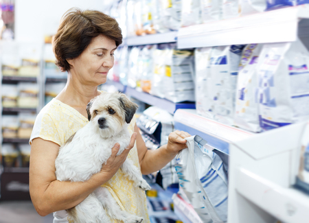 Elderly woman choosing dog food for her puppy in pet supplies storeの写真素材
