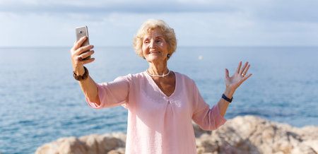 Smiling senior lady relaxing on beach walk and making selfie