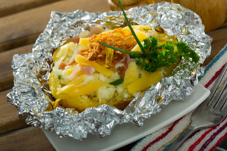 Tasty cooked in foil baked potato filled of salad with cheese, bacon and fried onionの写真素材