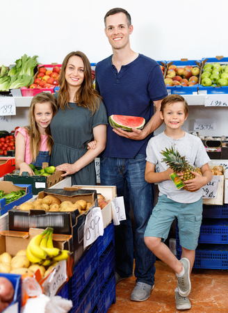 Smiling  positive glad  family with kids showing fresh delicious fruits during family shoppingの写真素材