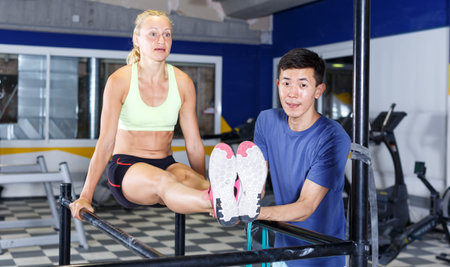 Young female athlete doing push-up on horizontal bars at gym with male instructor