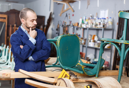 Professional young man carpenter repairing antique furniture in workshopの写真素材