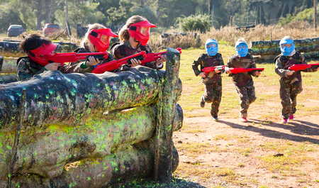 Two opposing teams of kids shooting on paintball playing field outdoorsの写真素材