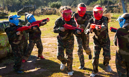 Two opposing teams of active kids shooting on paintball playing field outdoorsの写真素材