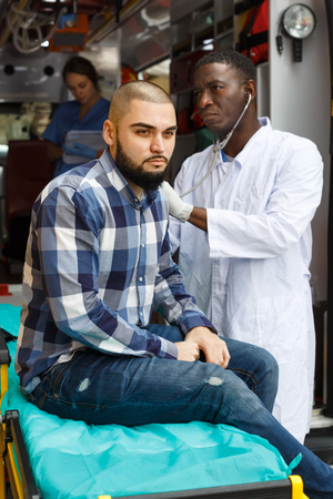 ambulance team providing medical care to upset male patient in ambulance car outdoorの写真素材