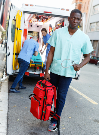 Three positive glad pleasant efficient ambulance doctors posing in ambulance car with medical equipmentの写真素材