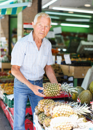 Positive senior man searching for fresh fruits in greengroceryの写真素材