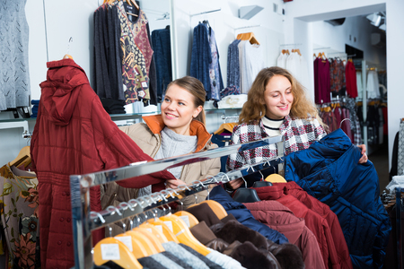 Portrait of two young attractive women choosing new overcoat in clothing storeの写真素材