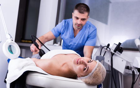Young woman getting machine cosmetological body procedure in modern aesthetic clinicの写真素材